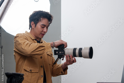 Bild auf Leinwand Asian male photographer adjusting professional camera with telephoto lens in stu