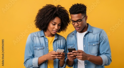 Young african american couple looking at their smartphones against yellow background