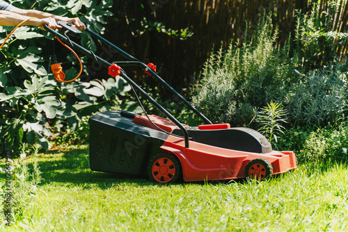 Foto Red electric lawn mower on a vibrant green grass in a beautiful summer garden