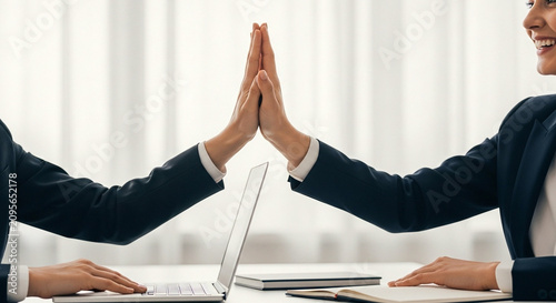 Two colleagues giving a high five over a laptop in celebration