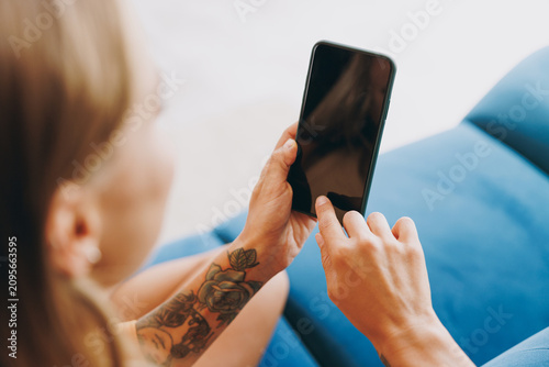 Cropped young woman wears casual clothes hold use mobile cell phone with blank screen workspace area sits on blue sofa couch stay at home hotel flat rest relax spend free time in living room indoor.