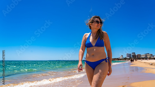 Картината върху платно Beautiful middle-aged woman sunbather walking on sandy beach in summertime