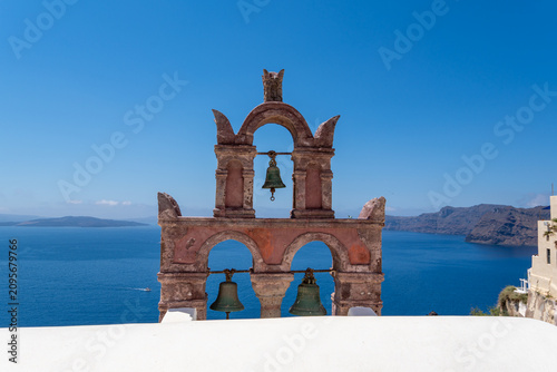 Konstfotografi Traditional pink stone bell tower with three bells under a clear blue sky in Oia, Santorini