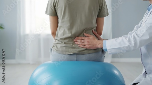Doctor examining patient back pain on exercise ball in clinic