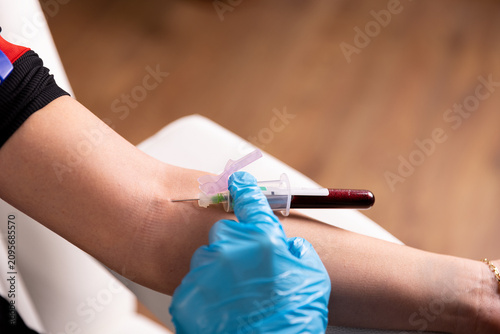 Close-up of a doctor or phlebotomist taking a blood sample into a vacuum tube from a patient's arm vein during venipuncture.