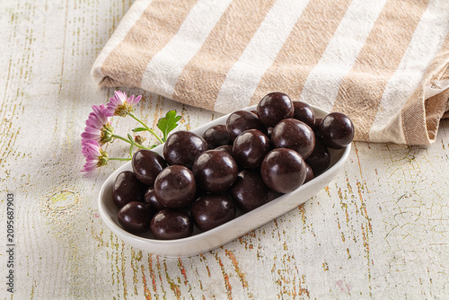 Bild auf Leinwand Dark chocolate coated candies in white dish with purple flowers on rustic table