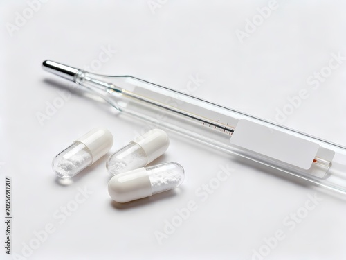 Close up of a clinical glass thermometer alongside several white capsules representing healthcare and medical diagnostic monitoring