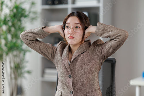 Fotografie Young businesswoman with eyeglasses covering her ears, experiencing headache and