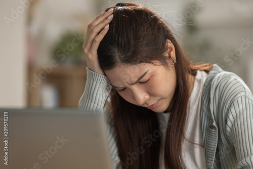 Fotografie Stressed tired young asian woman holding head feeling headache sitting at home w