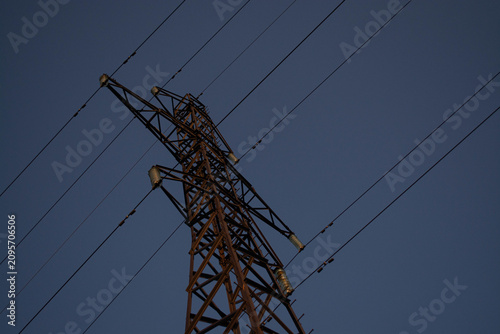 High voltage electric pylon against clear blue sky at sunset. Metal transmission tower with power lines for electrical energy supply and industry infrastructure grid distribution.