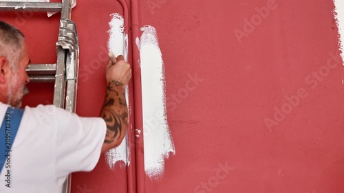 Tattooed painter painting red wall white