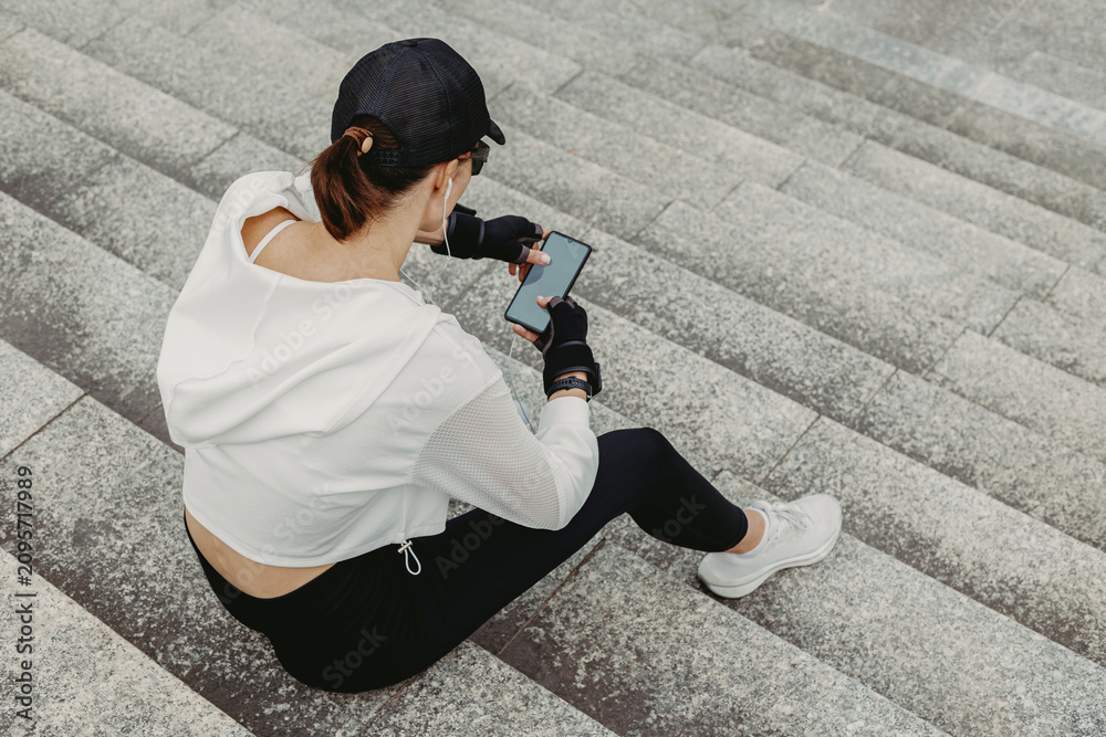 Obraz premium Young woman checking phone while seated on concrete stairs