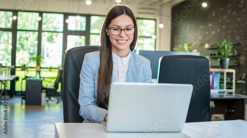 Cuadro en lienzo Content young businesswoman wearing glasses and working on laptop in spacious op