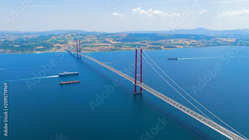 Lapseki, Turkey. 1915 Canakkale Bridge with moving cars above and multiple cargo ships and a passenger ferry on the Dardanelles below. Aerial View