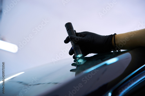 Fényképezés Professional mechanic examines a vehicle window by shining a flashlight on a gla