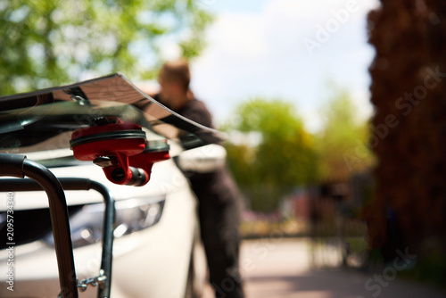 Red vacuum lifter holds new transparent car glass securely on an outdoor repair stand for mobile windshield replacement