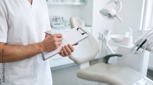 Medical professional writing on clipboard in modern dental clinic
