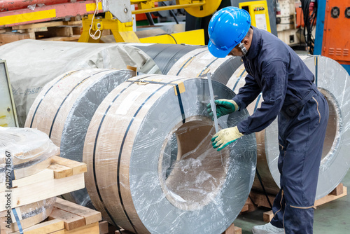 Technician industrial worker inspecting aluminum metal sheet fabricating roll check stock materials in the steel coil storage area, rolls metal sheet high quality durable meet standards industry.