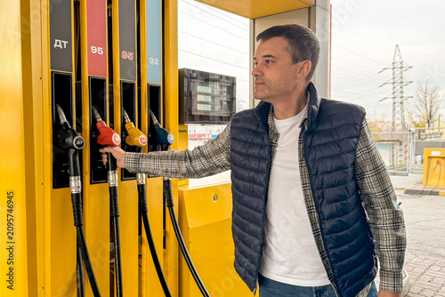 Foto Man selecting fuel pump at gas station with yellow dispenser and multiple octane