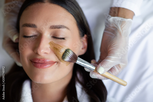 Foto Calm woman smiling during luxury facial procedure while beautician carefully spr