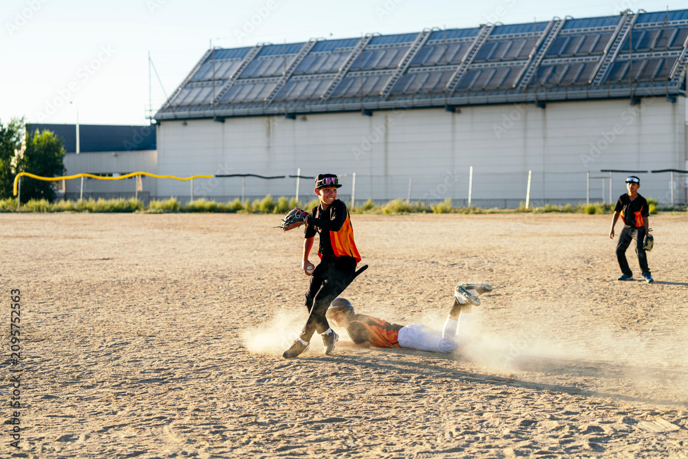 Obraz premium Young baseball players competing on a dusty dirt field, one sliding while defender attempts a tag out during a game
