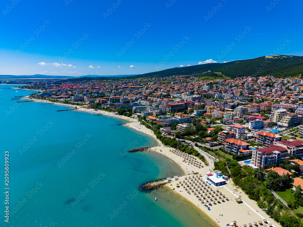 Fototapeta premium Coastal view of a city by the beach with clear water and green hills under a blue sky in the daytime