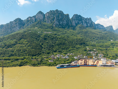 A cargo ship is docked along the river bank at the Three Gorges Reservoir in Yichang China under a bright blue sky with green mountain scenery