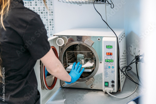 Medical worker in glove opens door of fractionated vacuum autoclave to load dental tools for sanitization. Autoclave sterilizer machine, dental sterilization equipment, medical autoclave technology.