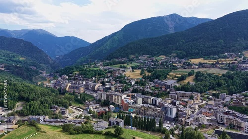 Aerial view of La Massana, Andorra, showing a dense alpine town with active construction cranes, chalet-style buildings, green forested Pyrenees mountains, and a wide valley