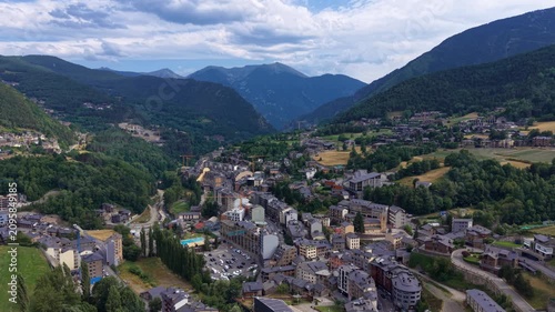 Aerial view of La Massana parish town, Andorra, showing dense urban residential buildings, swimming pool facility, and forested Pyrenean mountain valley under cloudy sky
