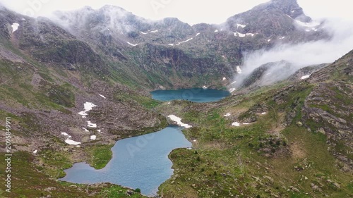 Two turquoise glacial lakes connected by a mountain stream in a rocky cirque, low clouds wrapping the peaks, snow patches on surrounding slopes, Tristaina Lakes, Andorra, Pyrenees