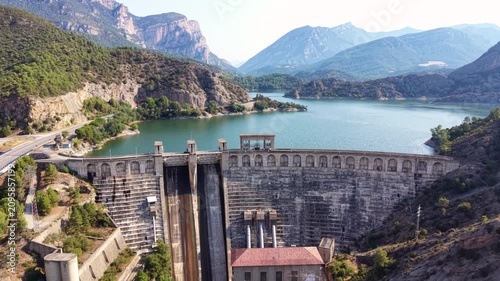 Aerial view of the arched facade and spillway of the Oliana hydroelectric dam with turquoise reservoir and mountain landscape, Segre River, Lleida, Catalonia, Spain