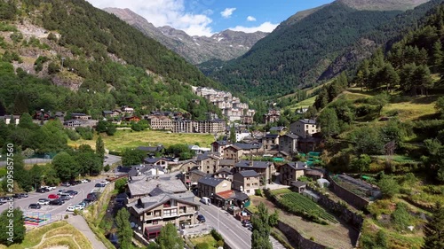 Aerial view of Arinsal village in Andorra featuring traditional stone and slate buildings, ski gondola on mountainside, terraced vegetable gardens, and snow-capped Pyrenees peaks in summer