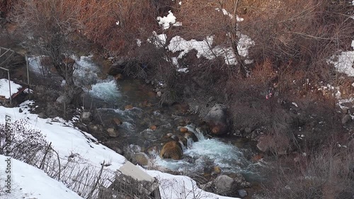 Top-down overview video with a view of a shallow narrow river with a 4-fold slower water flow with a blue tint, especially noticeable at the rapids. Winter landscapes in mountainous areas