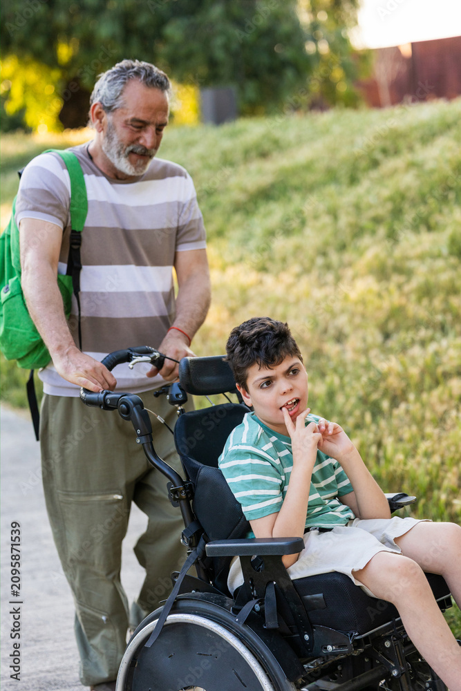 Obraz premium Grandfather pushing child with cerebral palsy in wheelchair