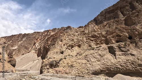 Tilt across an eroded cliff face riddled with ancient sky caves on the road to Chele, Upper Mustang, Nepal