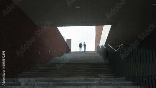 Two men climbing the stairs come out of the tunnel. Rear view