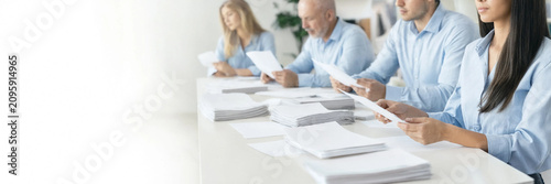 A team of office workers sorting and organizing stacks of paper at a long table. The group works collaboratively in a bright, minimal office with ample copy space on the left.