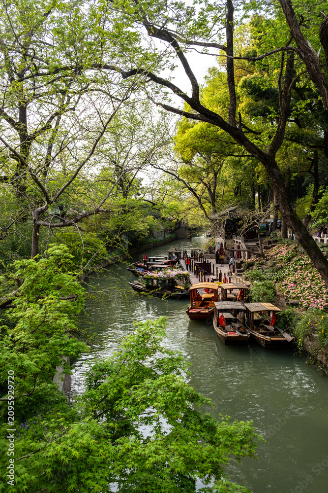 Fototapeta premium Canal boats beside spring trees and flower beds at Tiger Hill Park, Suzhou, China