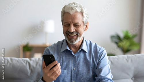 Older Man With Silver Hair Using Smartphone On A Couch In A Sunlit Living Room