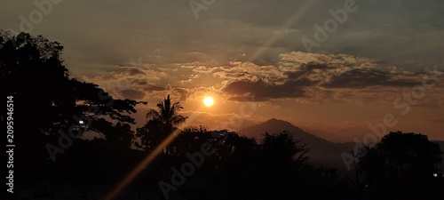 Photography A beautiful golden sunset shining over tropical mountains with dramatic clouds and silhouettes of trees