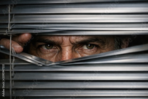 A close-up view of a person peeking through window blinds, with a hint of curiosity