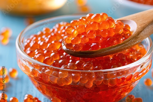 Red salmon caviar glistening in glass bowl with wooden spoon in sharp macro focus for gourmet seafood marketing