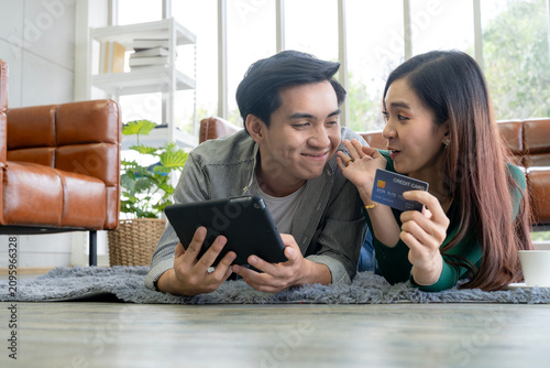 Cheerful man and woman smiling together while using a laptop and credit card for e-commerce purchase, representing smart consumer and safe digital payment.
