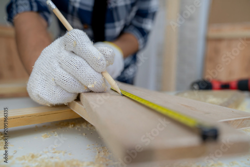 Detailed shot of a craftsman's hands using a measuring tape on timber, representing home DIY projects, woodworking skill, and carpentry concept.