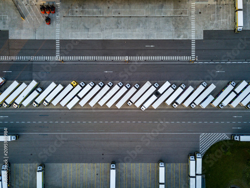 Fotografie Top down aerial view of many white semi trucks parked in a neat row at a modern logistics center, fleet management and global freight transportation concept