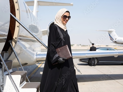 Successful Arab businesswoman in traditional abaya boarding a luxury private jet