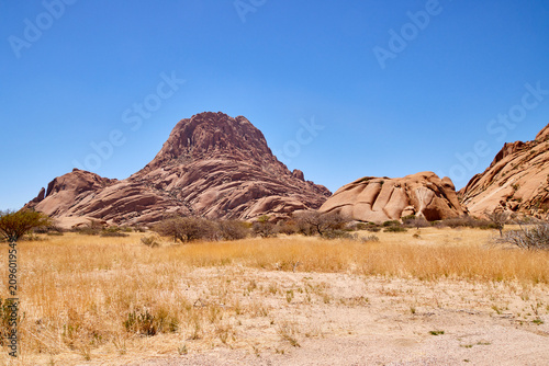 Foto Eine Felslandschaft mit Granitberg, trockener Ebene und blauem Himmel zeigt Spitzkoppe in Namibia