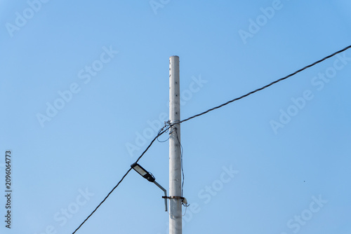 Utility pole with LED street light and overhead utility cables with clear blue sky background