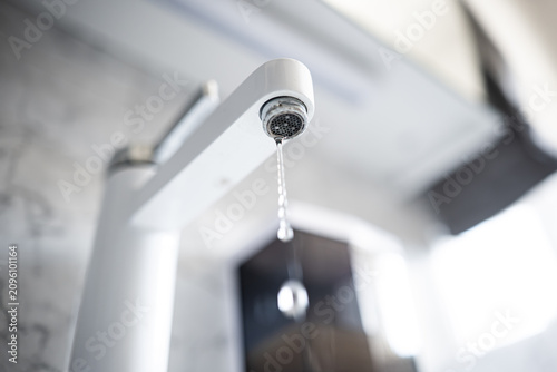 Low angle close up of a modern white tap faucet aerator with visible limescale build up in a bathroom